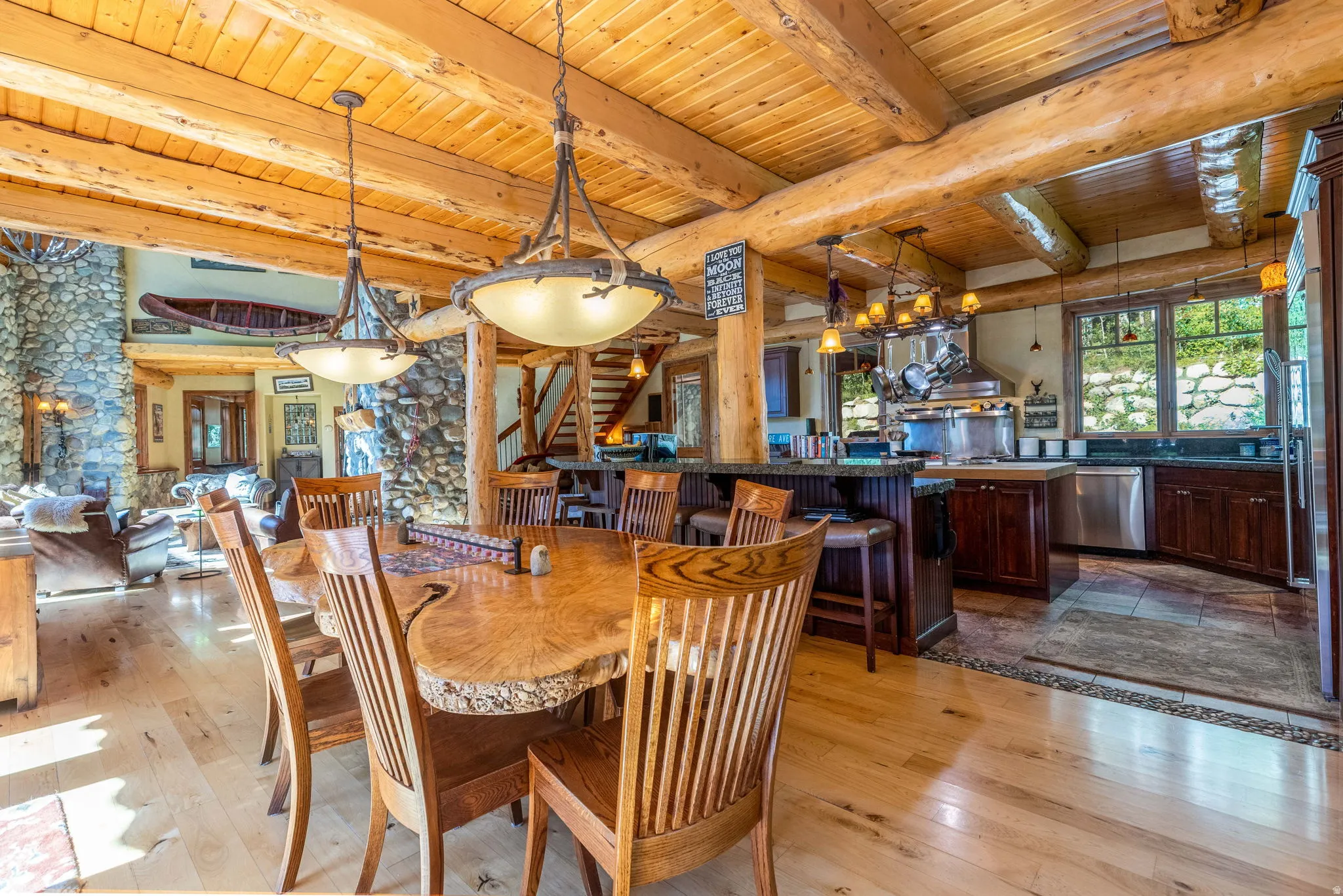 Expansive open-concept living space featuring wood-finish flooring, exposed wood beam ceiling, and a large stone-clad fireplace