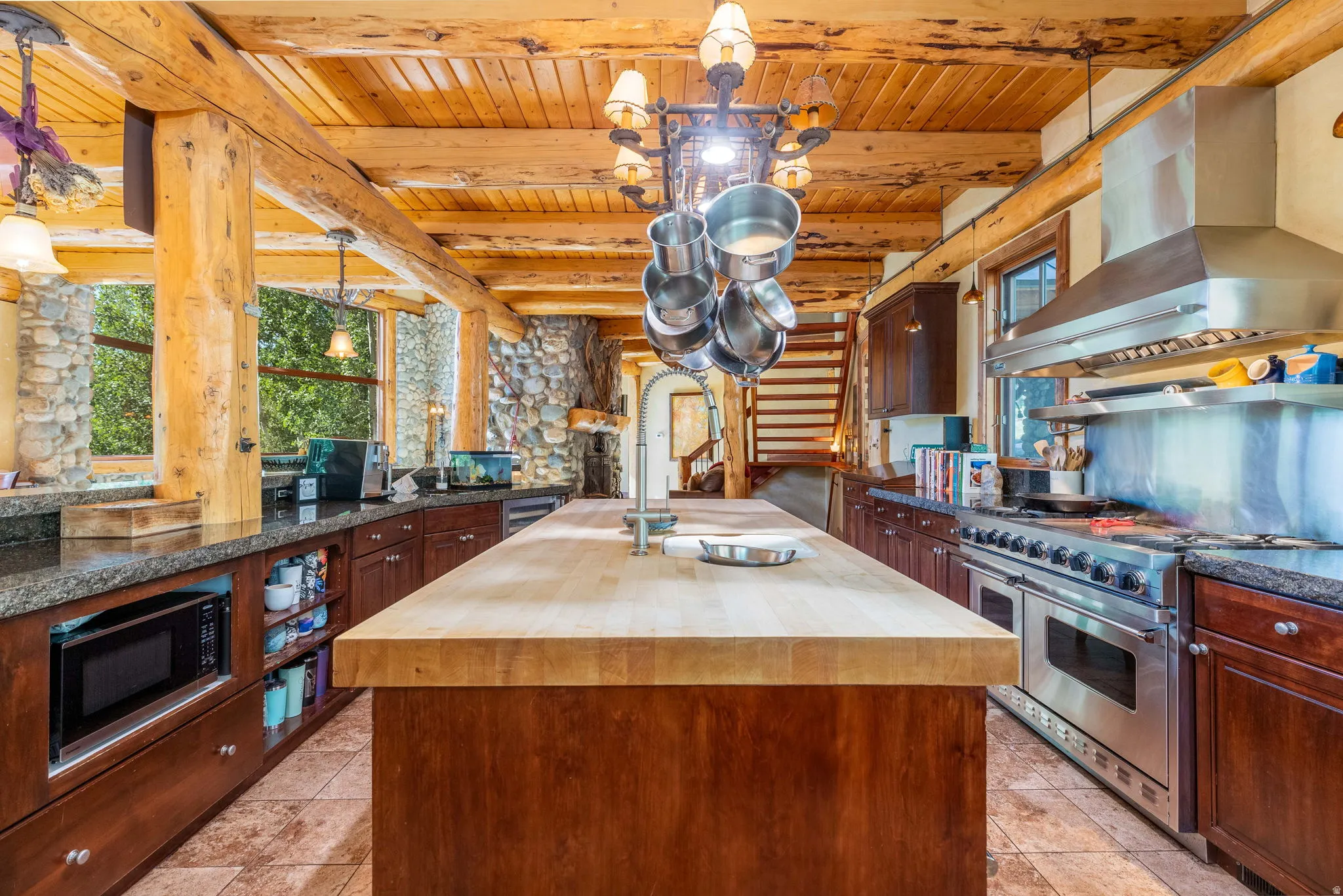 Kitchen featuring a large wood-finish island, professional-grade stainless steel range with matching hood, ample dark wood cabinetry, granite-style countertops, and exposed wood beams