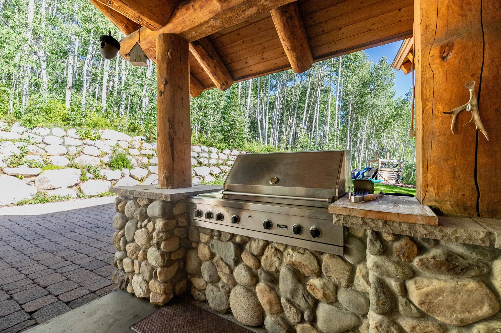 Outdoor kitchen featuring a built-in stainless steel grill set within a river stone base with a stone countertop.
