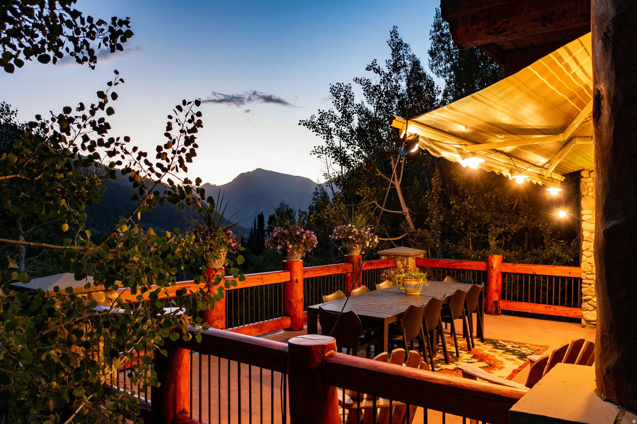 Expansive outdoor deck featuring a plank-style railing, mountain scenery, and an overhead awning with string lights
