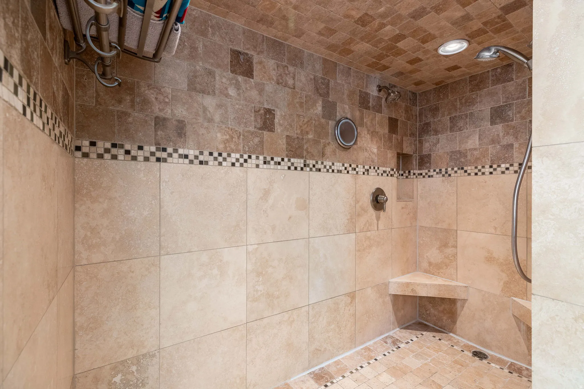 Spacious shower featuring multi-toned tile work, a built-in corner bench, a recessed niche, dual showerheads, and recessed lighting
