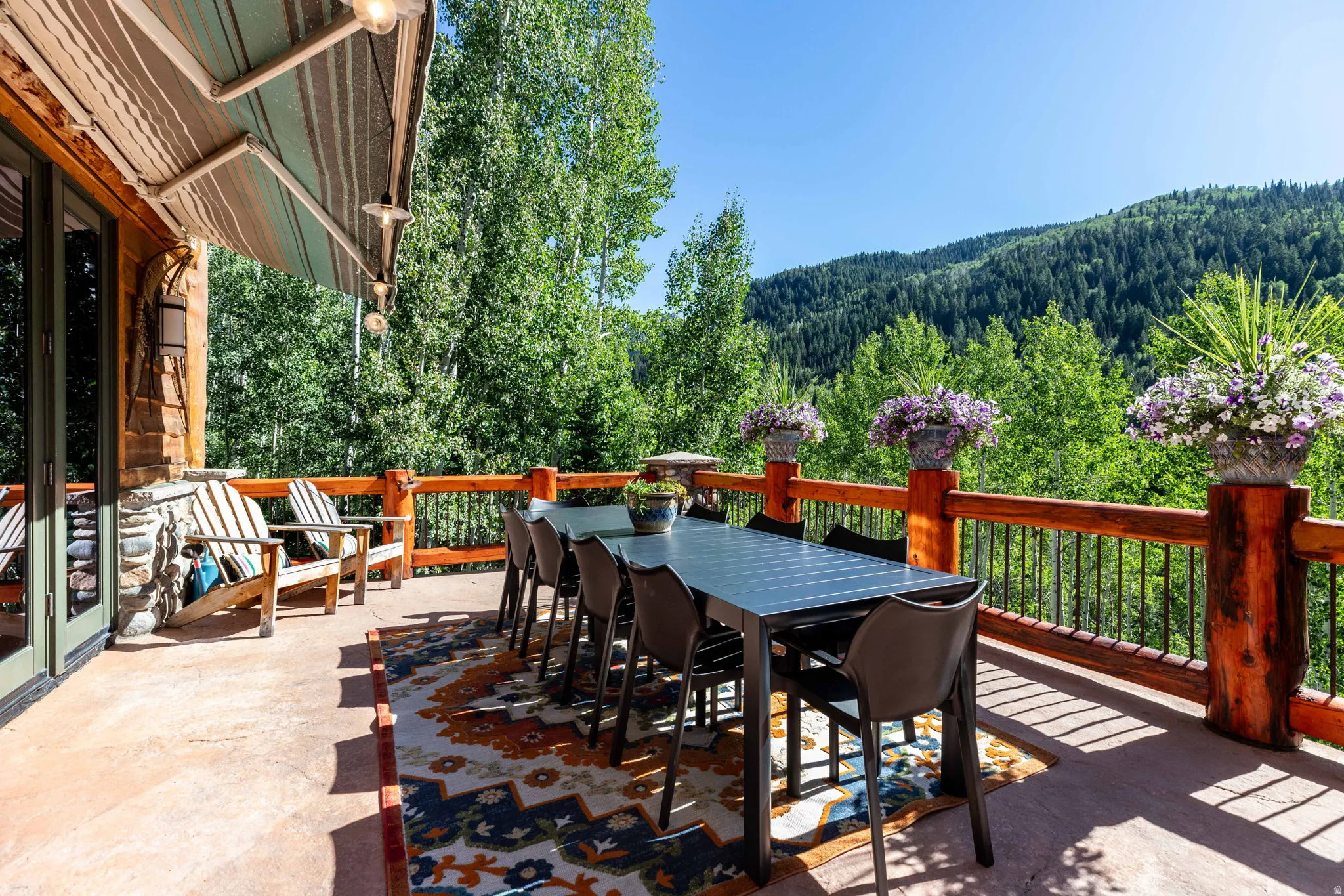 Expansive outdoor deck featuring a concrete surface, a striped retractable awning, and a robust wood railing with metal balusters