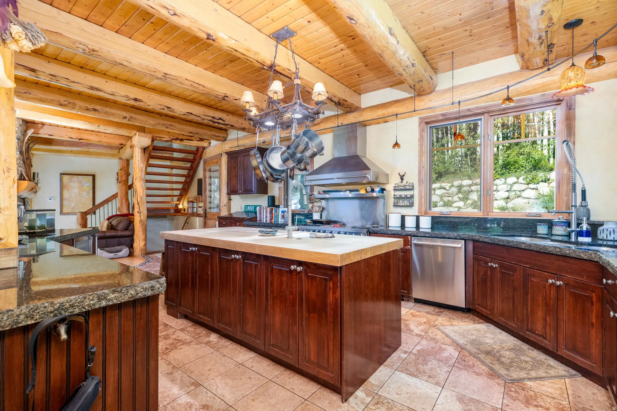 Spacious kitchen featuring an expansive center island, warm wood cabinetry, stone-finish countertops, and stainless steel appliances, all beneath a natural wood beam ceiling