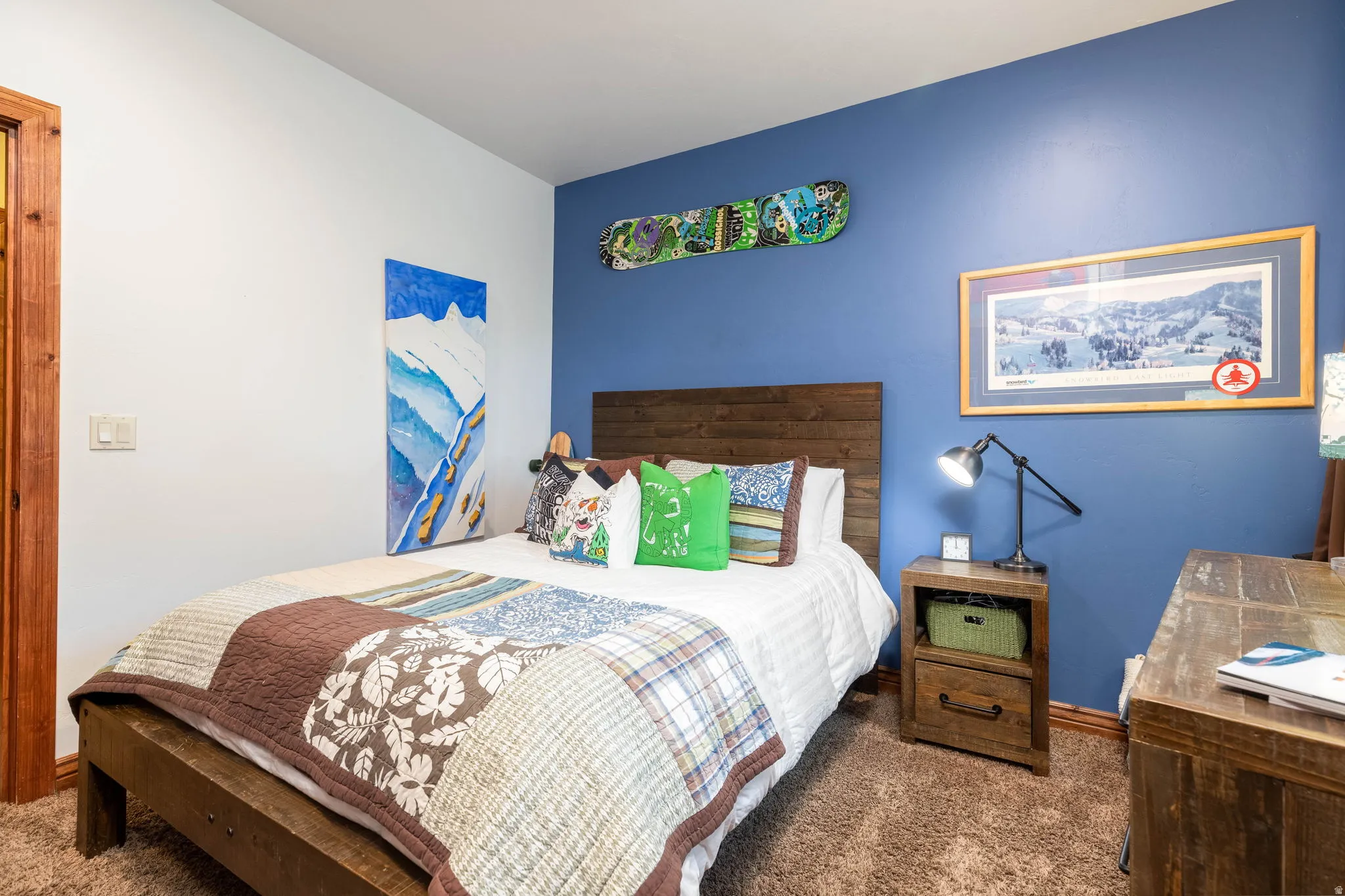 Bedroom featuring a rich blue accent wall, white painted walls, wood-finish flooring, and a wood bed frame with a matching headboard