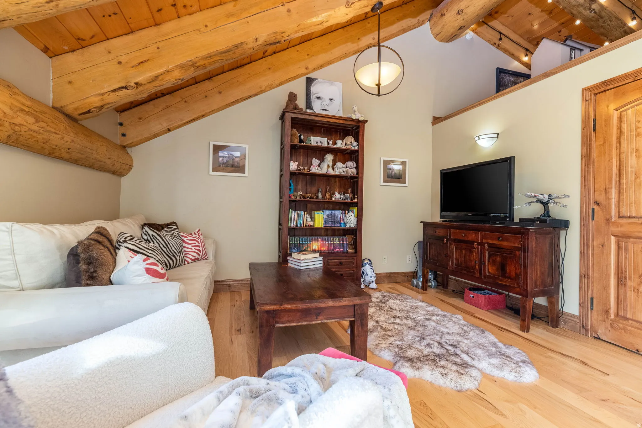 Vaulted ceiling with exposed wood beams, natural wood flooring, a built-in wall sconce, and a natural wood door