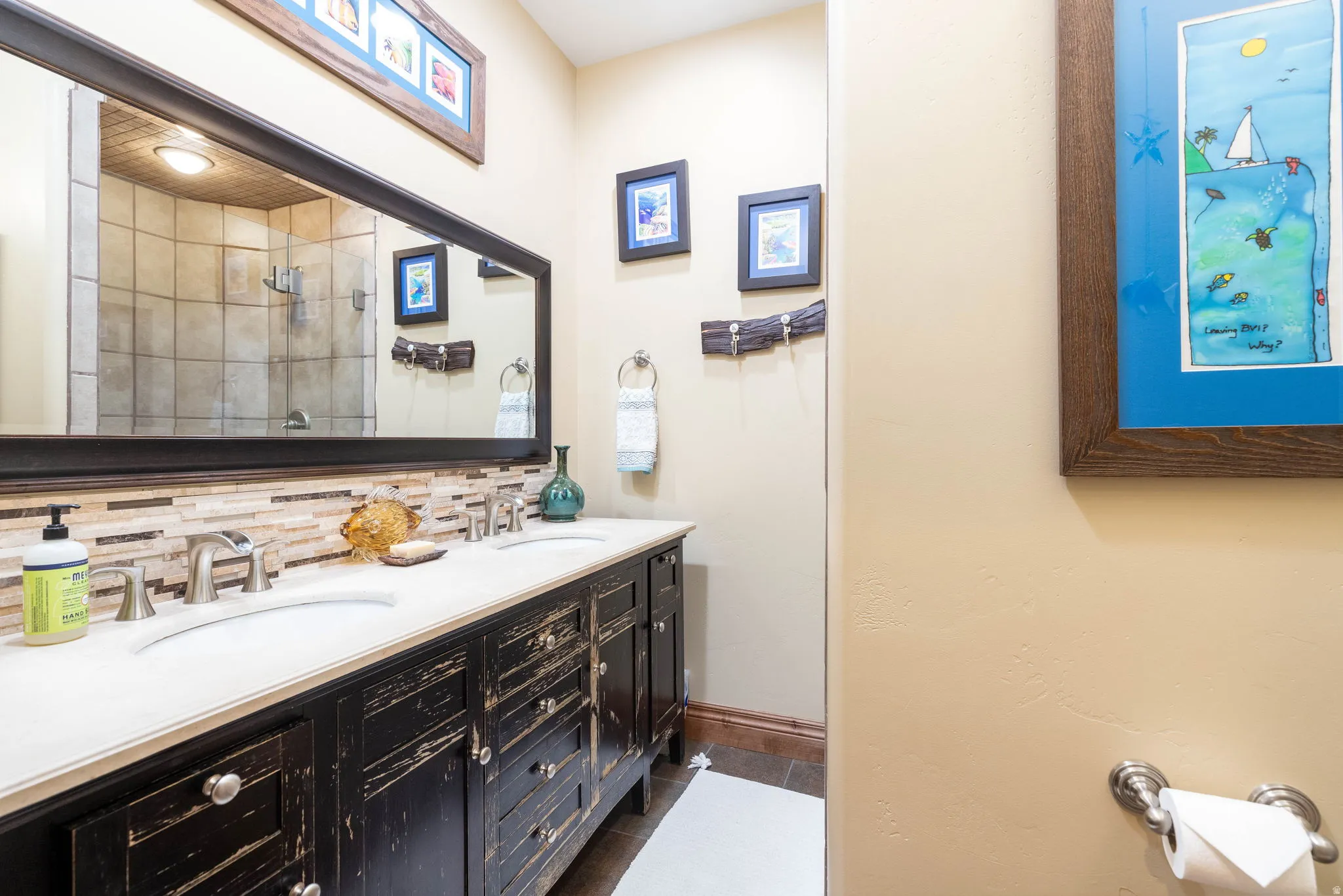 Dual sink vanity with distressed black cabinetry, light-toned countertop, and mosaic tile backsplash