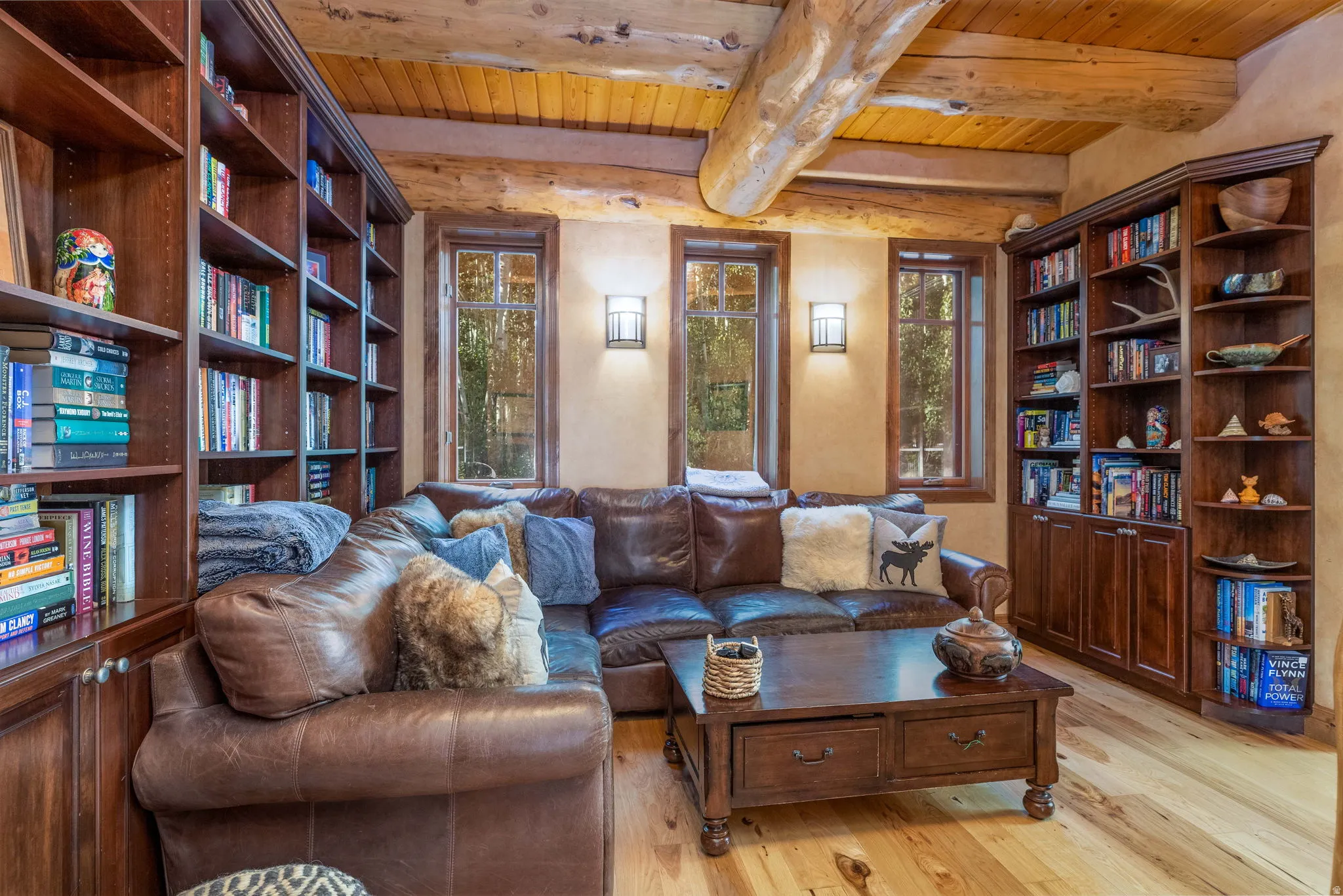 Living area featuring natural wood flooring, exposed timber beams, built-in custom wood shelving, and three vertical windows