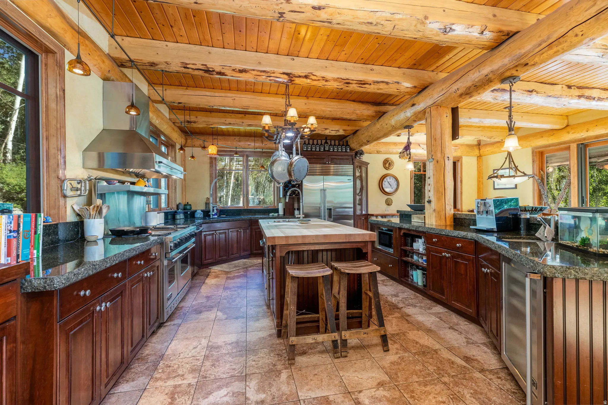 Spacious kitchen featuring a large wood-beam ceiling, wood-finish cabinetry, stone tile flooring, and stainless steel appliances