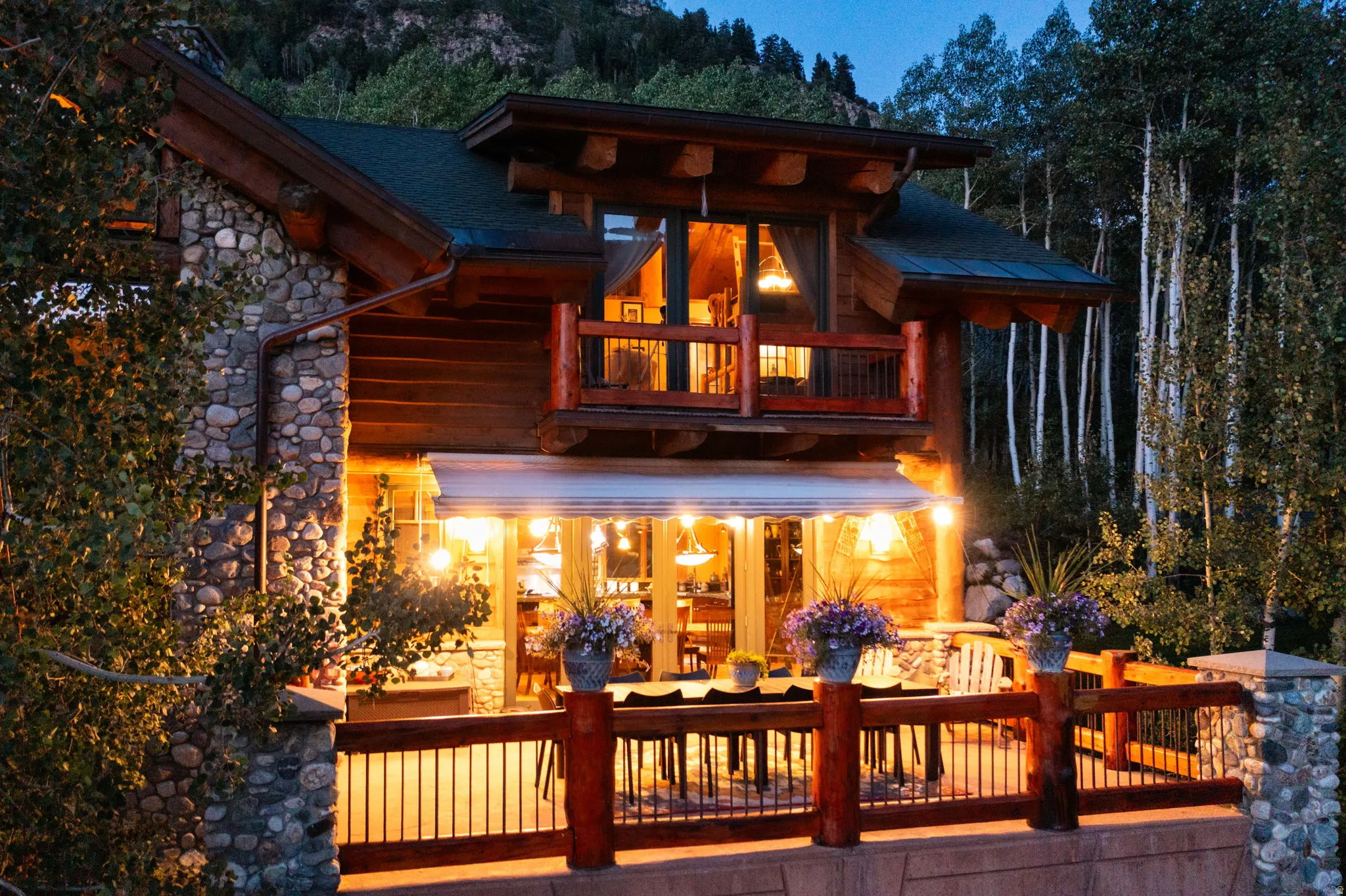 Stone and timber exterior featuring a lower-level patio with an awning, a second-story balcony, and a prominent peaked roofline