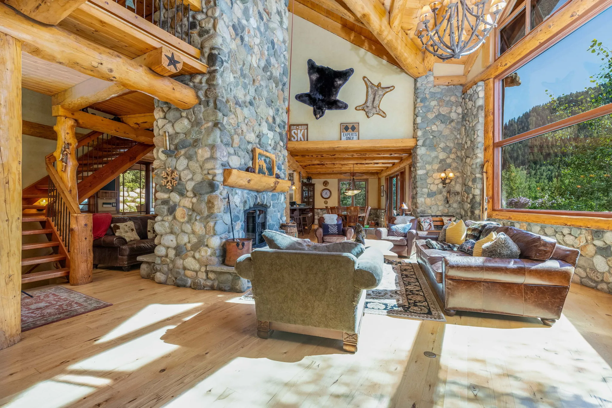 Grand living area featuring a stone fireplace with a wood mantle, exposed timber beams, a spiral wood staircase, and expansive windows