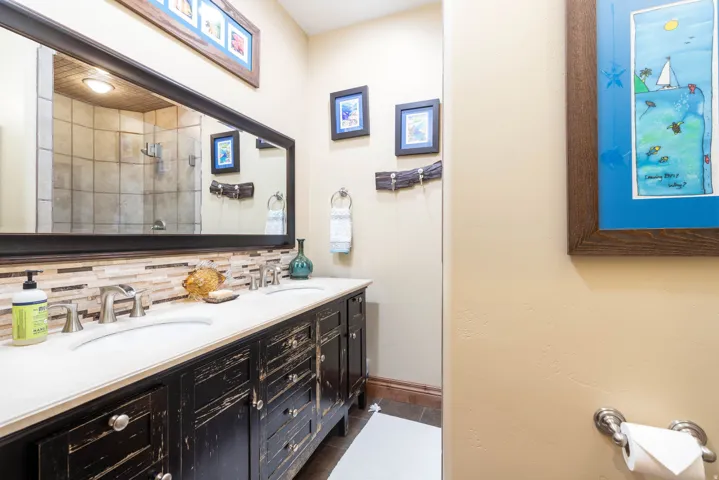 Dual sink vanity with distressed black cabinetry, light-toned countertop, and mosaic tile backsplash
