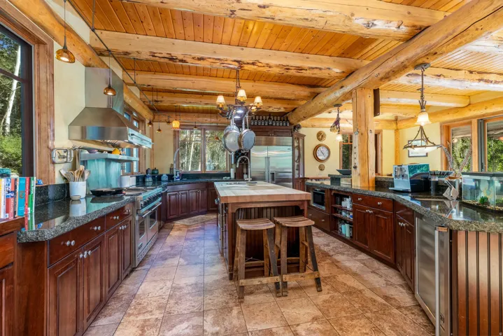 Spacious kitchen featuring a large wood-beam ceiling, wood-finish cabinetry, stone tile flooring, and stainless steel appliances