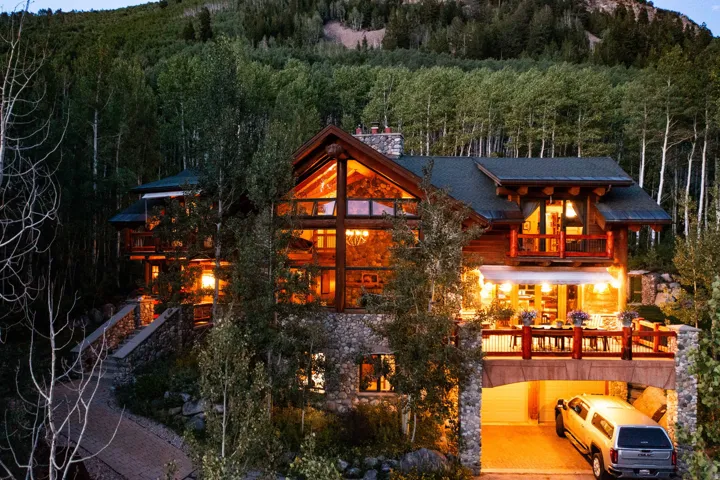 Stone and timber-frame residence featuring multiple levels, a prominent stone chimney, and an expansive deck with a white awning