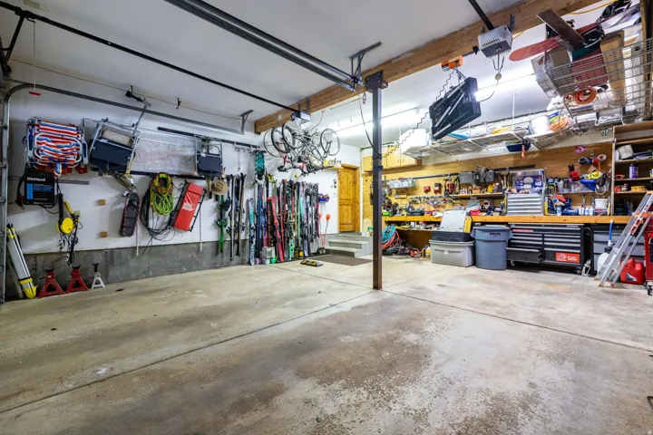 Spacious garage featuring concrete flooring, exposed wood beams, and an integrated workbench