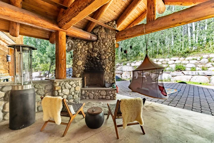 Spacious covered patio featuring exposed log beams, a stone fireplace, and a stone accent wall with built-in countertop