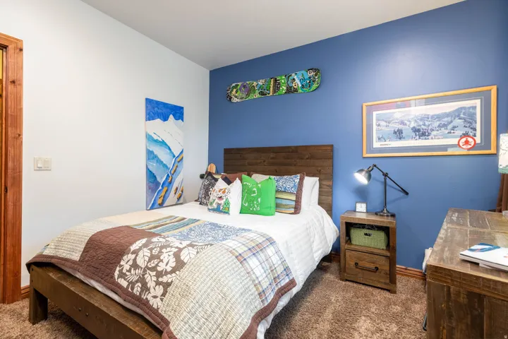 Bedroom featuring a rich blue accent wall, white painted walls, wood-finish flooring, and a wood bed frame with a matching headboard