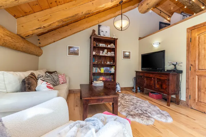 Vaulted ceiling with exposed wood beams, natural wood flooring, a built-in wall sconce, and a natural wood door