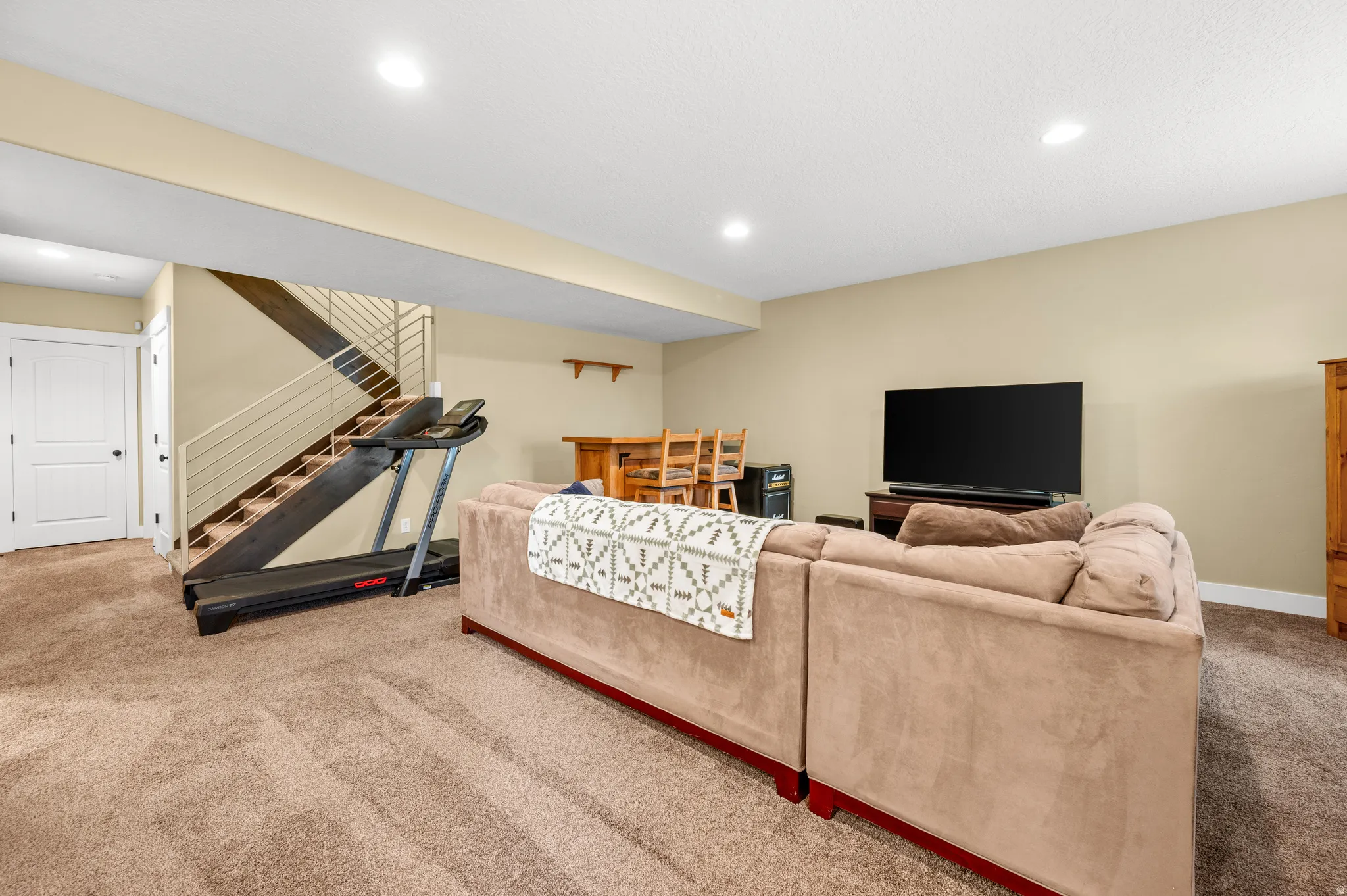 Carpeted lower-level space featuring recessed lighting, a two-panel door, and a staircase with open risers and metal railings