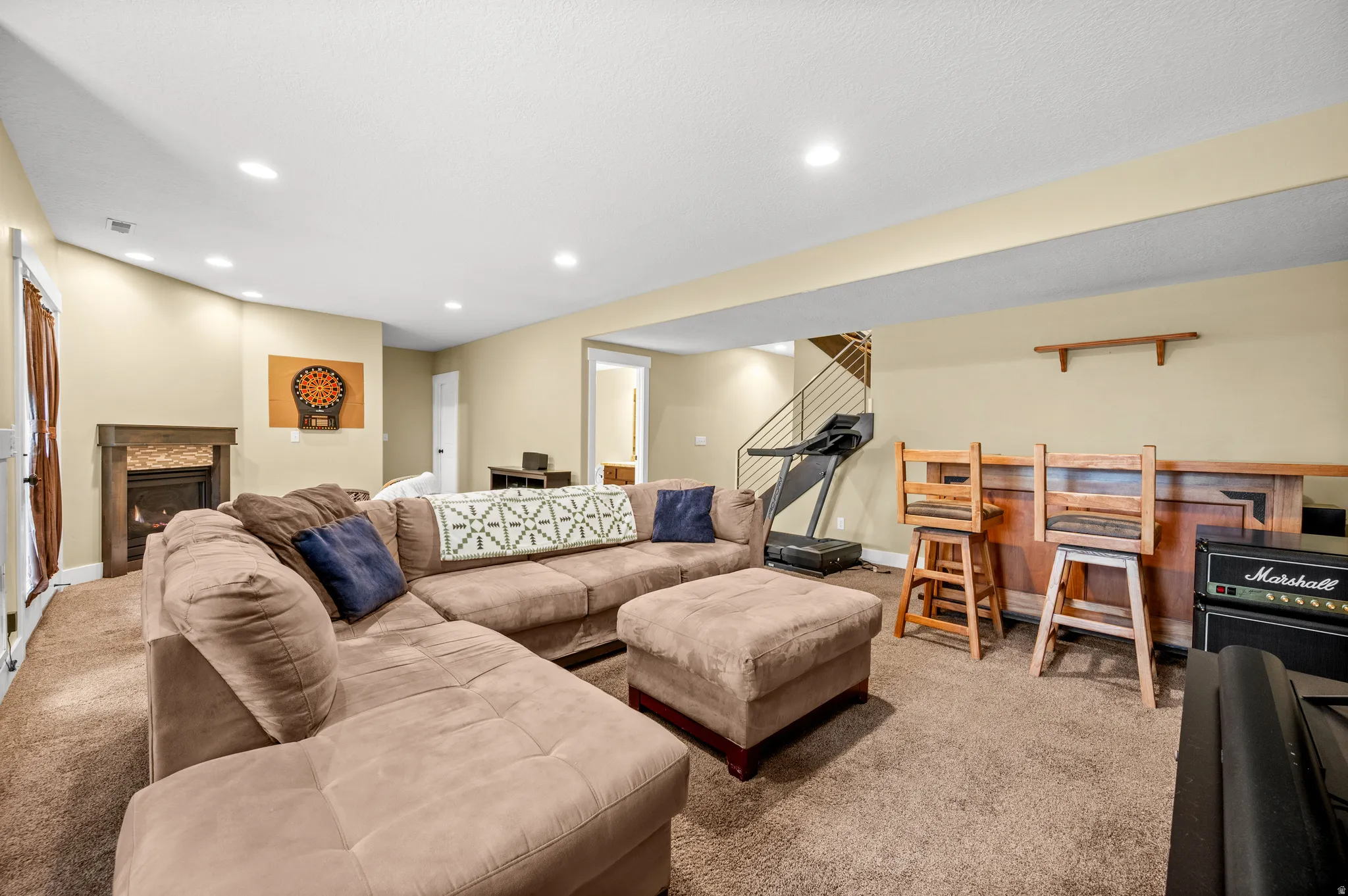 Spacious lower-level area featuring recessed lighting, a stone-clad fireplace with a wood mantel, and carpet flooring