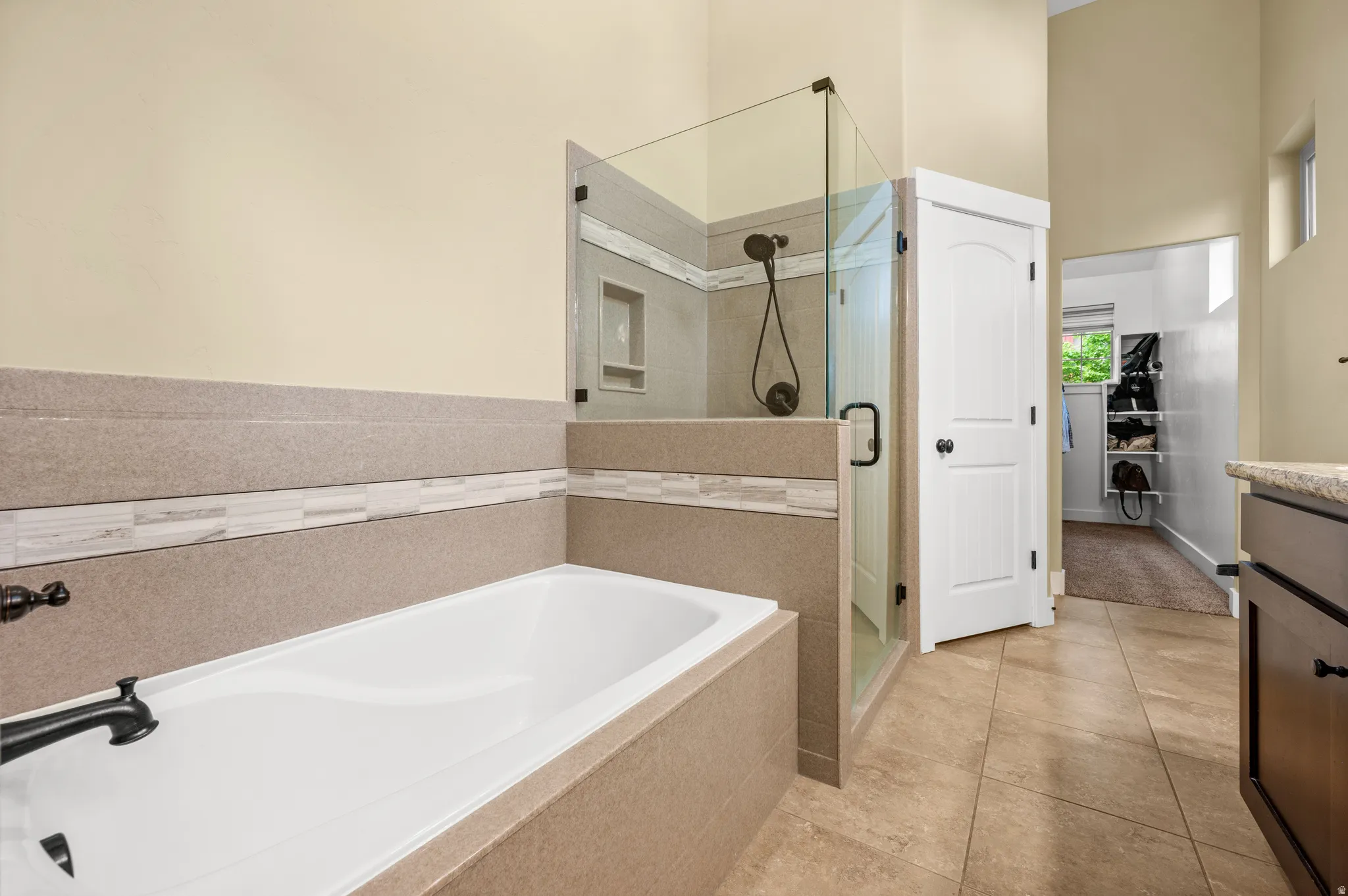 Spacious newly renovated master bathroom featuring a built-in soaking tub, a frameless glass shower enclosure with tile surround and niche, and tile flooring