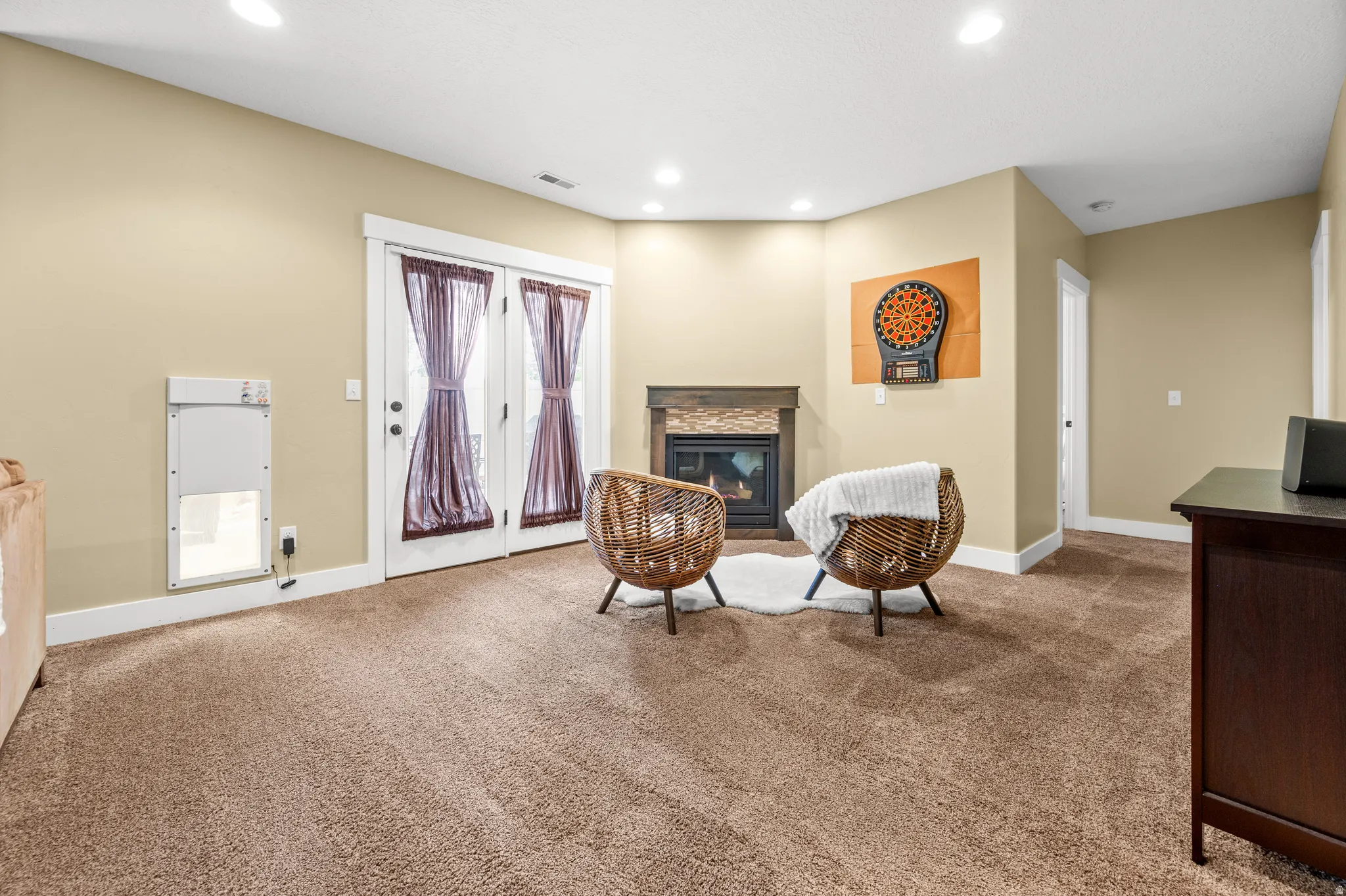 Cozy living area featuring plush carpet flooring, a corner fireplace with a stacked stone facade and wood mantel, recessed lighting, and French doors leading outdoors