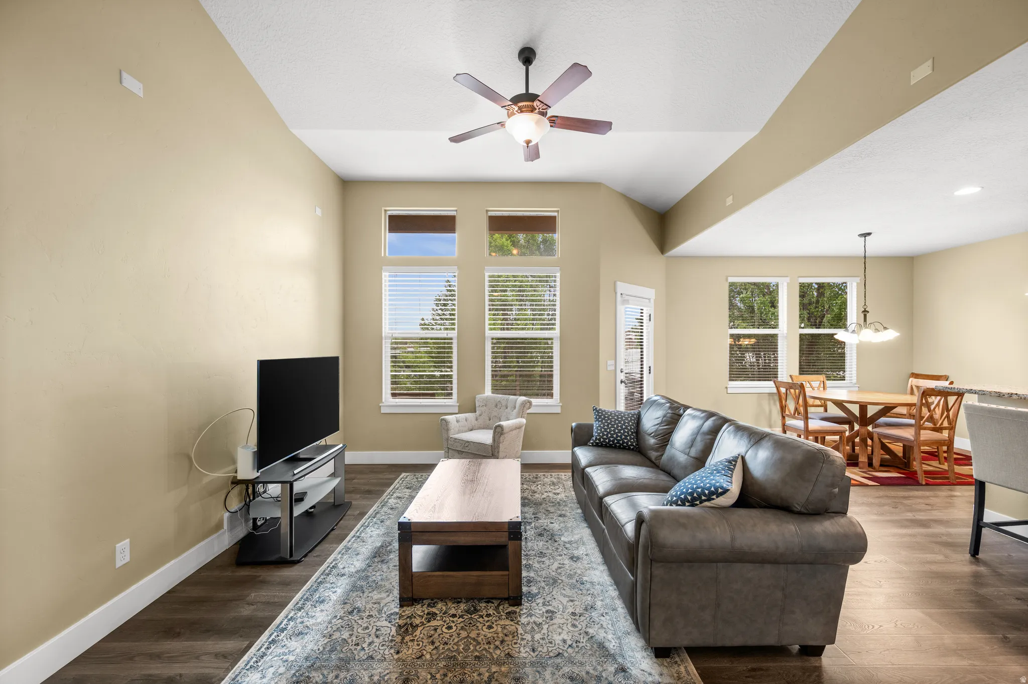 Vaulted ceilings with a ceiling fan, wood-finish flooring, and ample natural light from multiple windows
