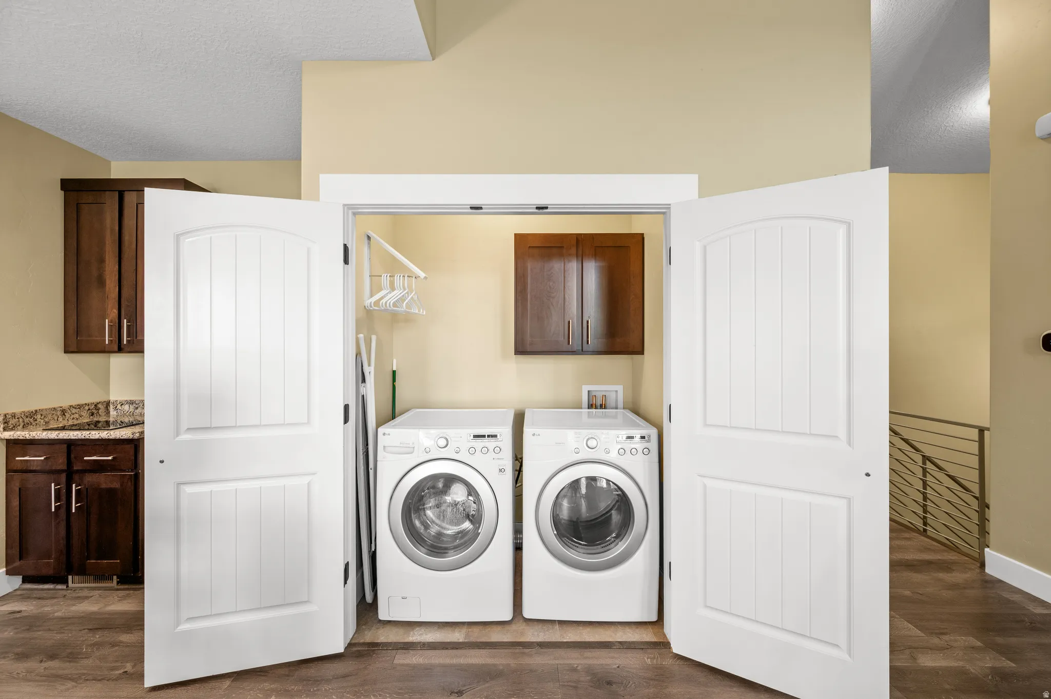 Laundry closet with double bifold doors, front-loading washer and dryer, and upper cabinetry