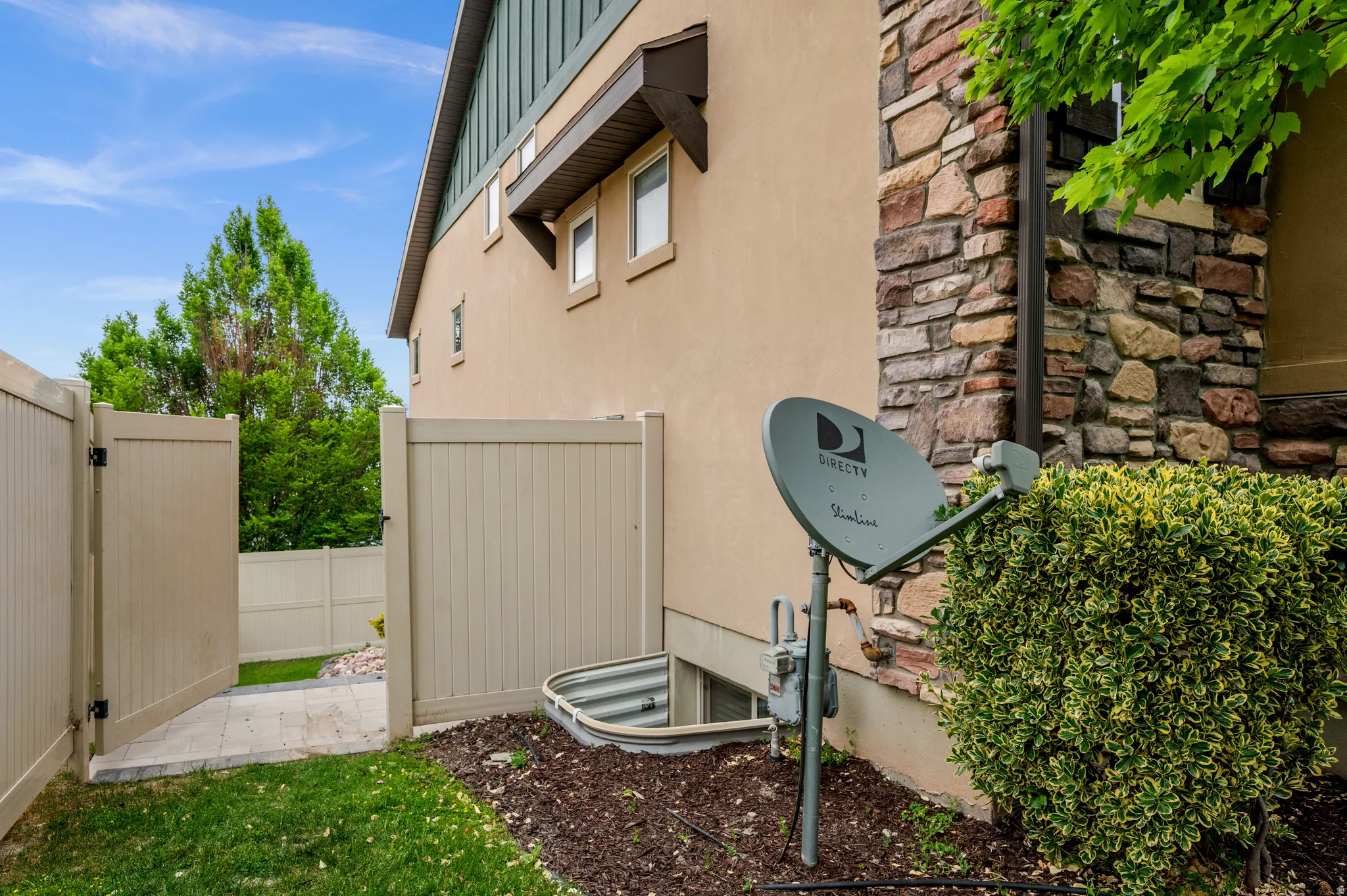 Private fenced side yard featuring a light-colored vinyl fence and gate, a window well, and a stucco and stone exterior
