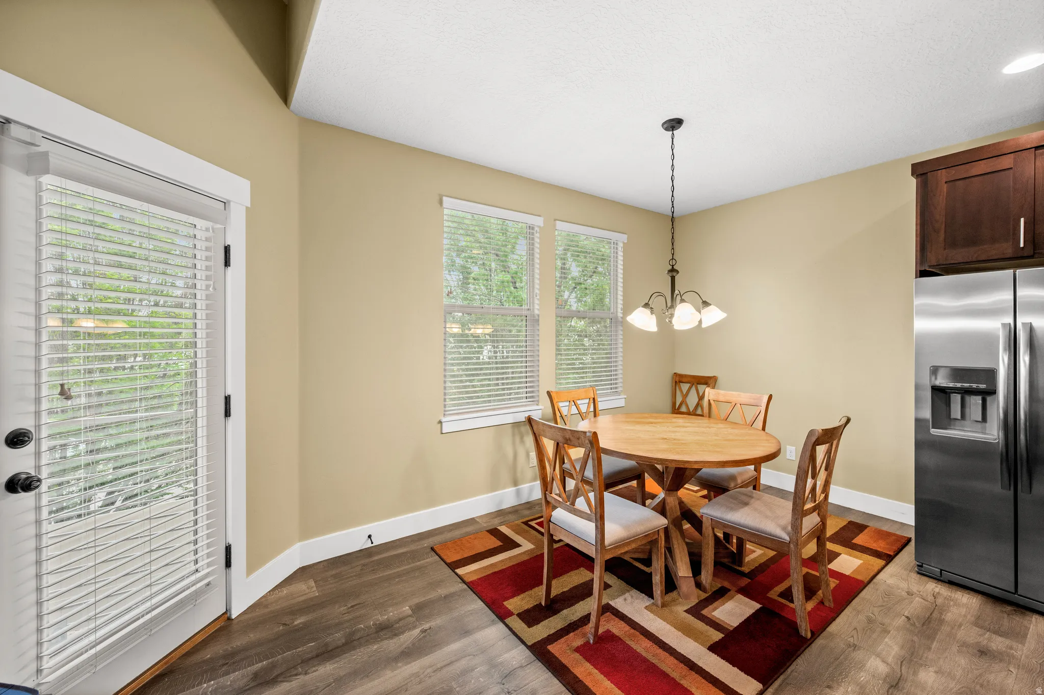 Dining area featuring wood-finish flooring, two windows with blinds, and a door with integrated blinds leading to the balcony