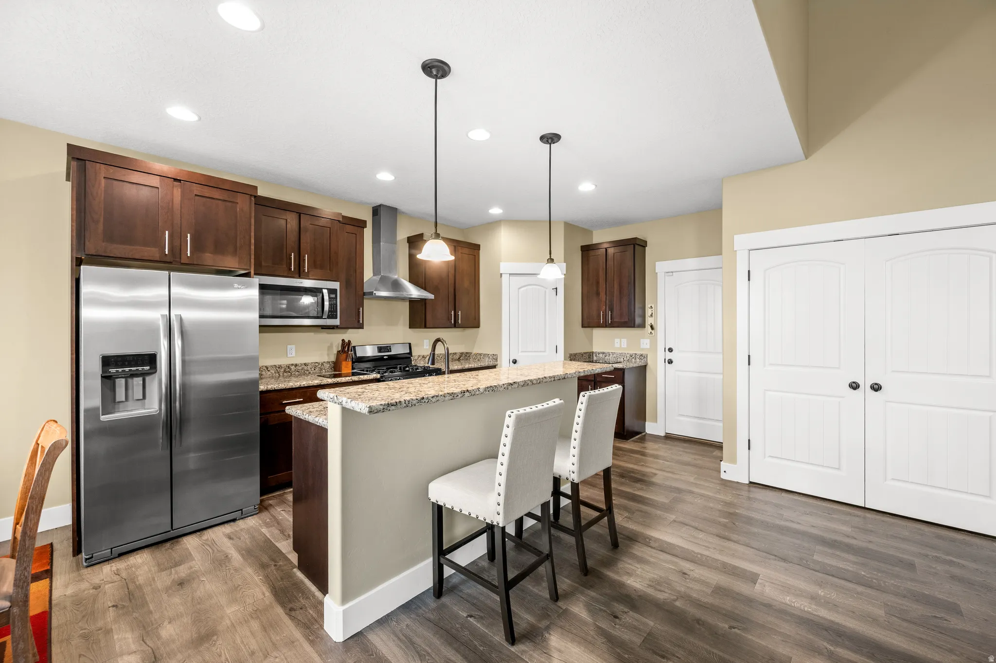 Kitchen featuring wood-finish flooring, stainless steel appliances, granite countertops, dark wood cabinetry, and recessed lighting