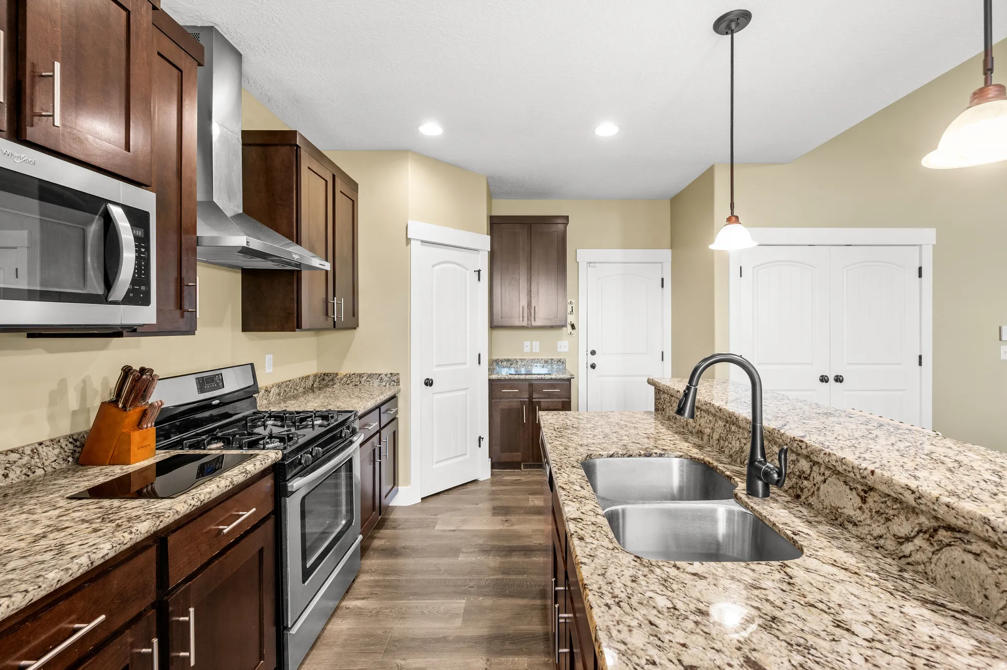 Kitchen featuring granite countertops, dark wood cabinetry, stainless steel appliances, and wood-finish flooring