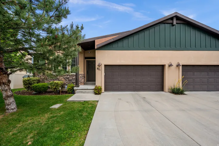 Stucco exterior with stone accents, featuring a two-car garage, mature landscaping, and a covered entry