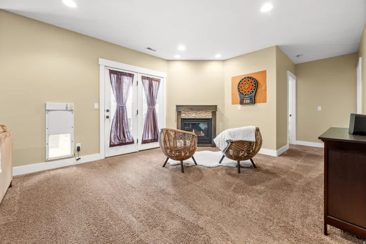 Cozy living area featuring plush carpet flooring, a corner fireplace with a stacked stone facade and wood mantel, recessed lighting, and French doors leading outdoors