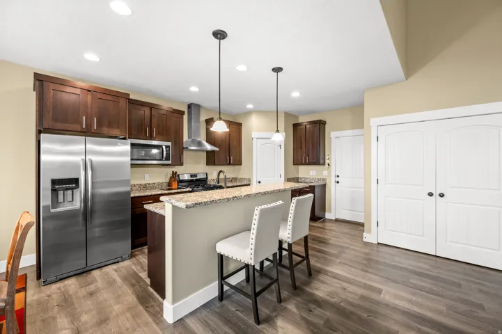 Kitchen featuring wood-finish flooring, stainless steel appliances, granite countertops, dark wood cabinetry, and recessed lighting