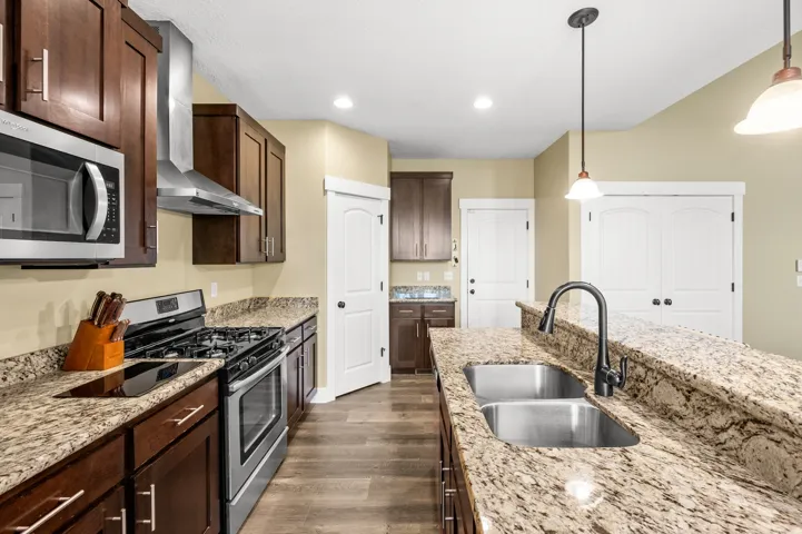 Kitchen featuring granite countertops, dark wood cabinetry, stainless steel appliances, and wood-finish flooring