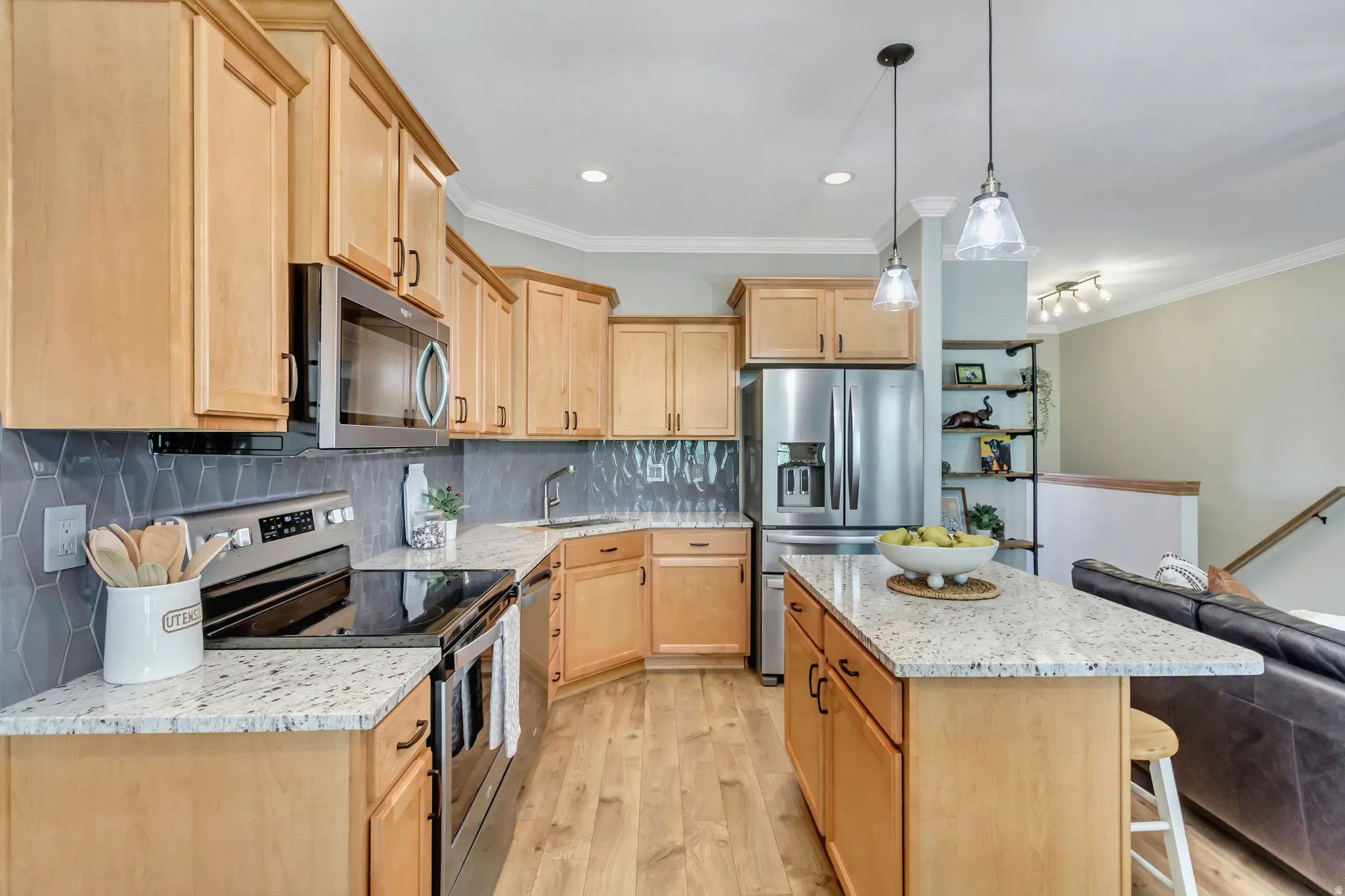 Kitchen featuring wood-finish flooring, light wood cabinetry, stainless steel appliances, tile backsplash and granite countertops
