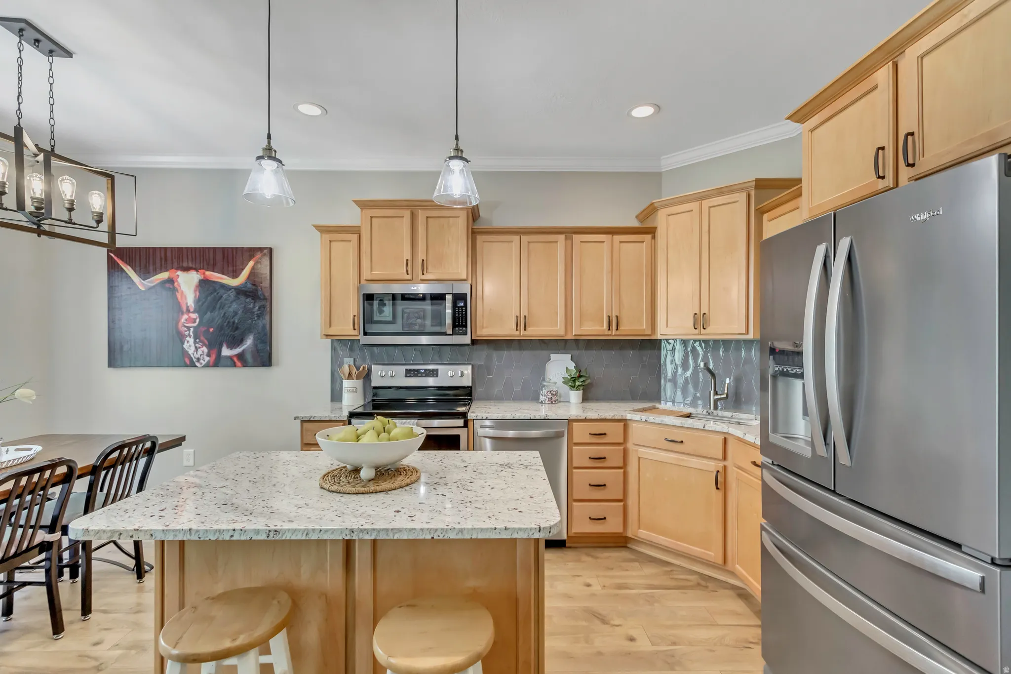Kitchen featuring an island with stone-finish countertop, light wood-finish cabinetry, stainless steel appliances, and wood-finish flooring
