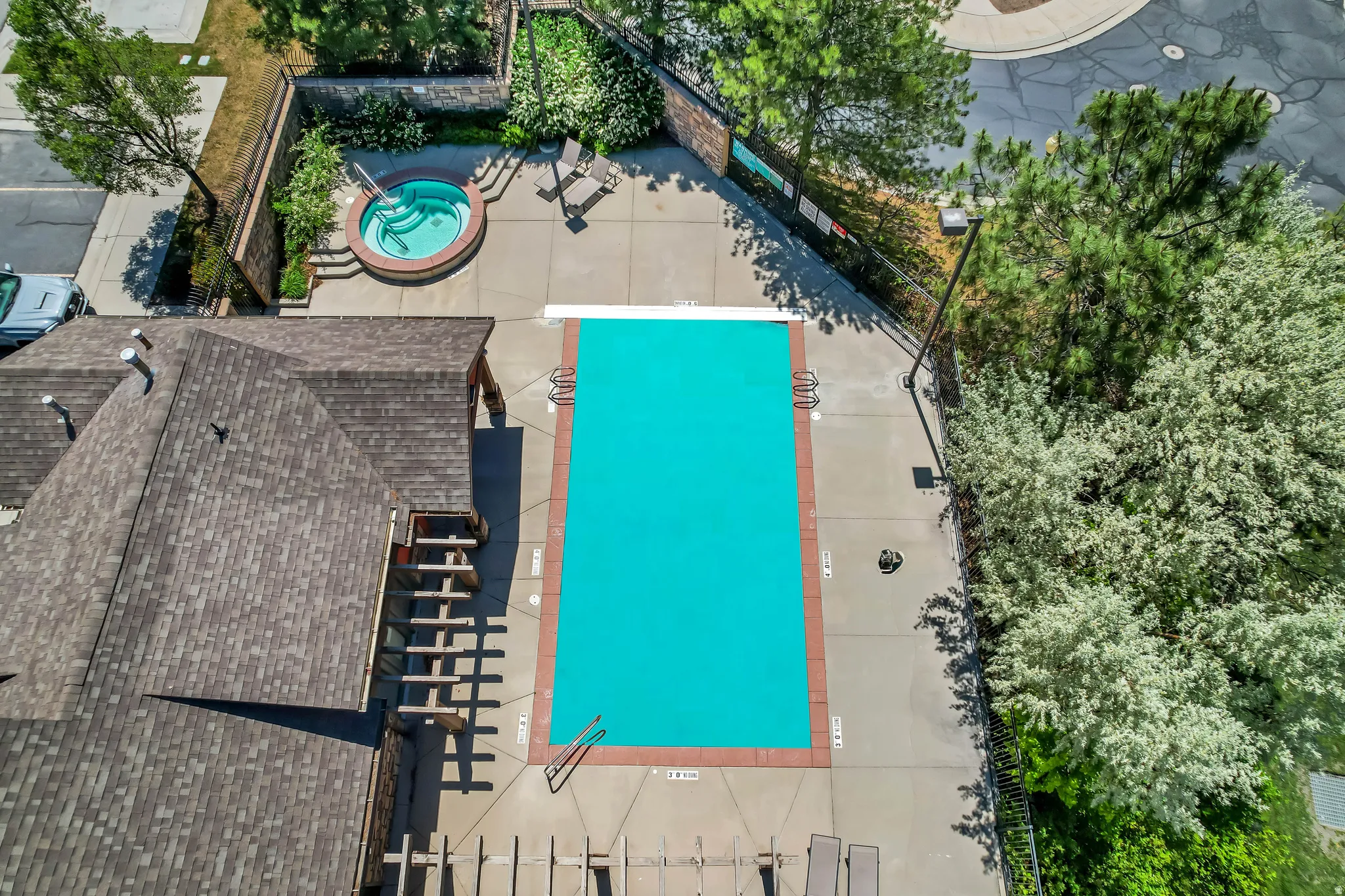 Outdoor swimming pool with surrounding concrete decking, integrated hot tub, and mature landscaping