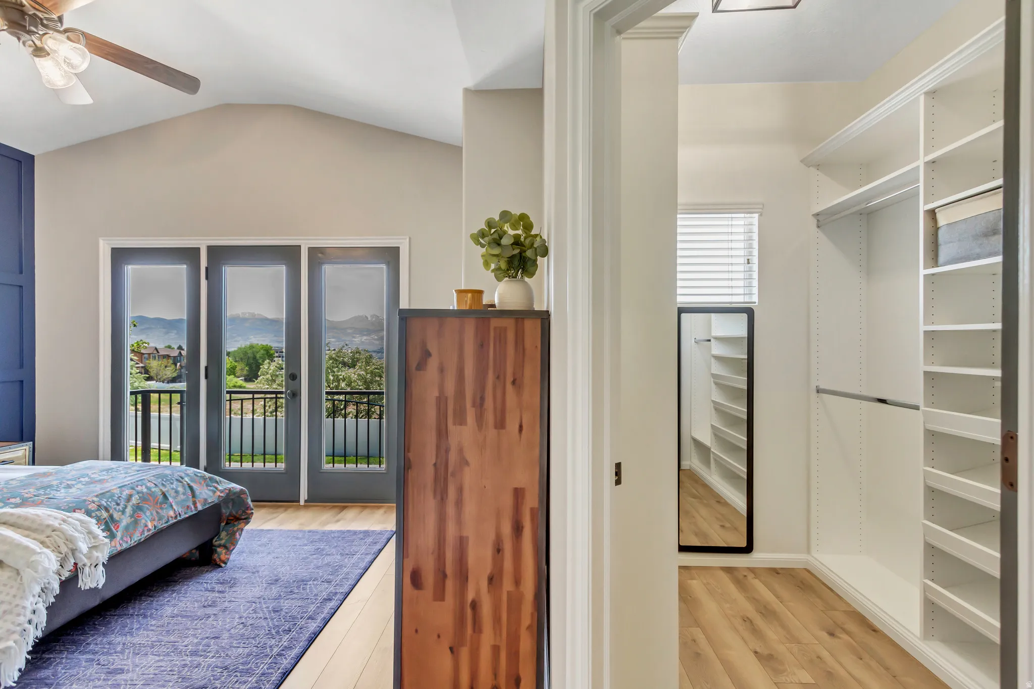 Spacious room featuring vaulted ceilings, wood-finish flooring, a ceiling fan, and a three-panel glass door opening to a private balcony all adjacent to roomy walk in closet.