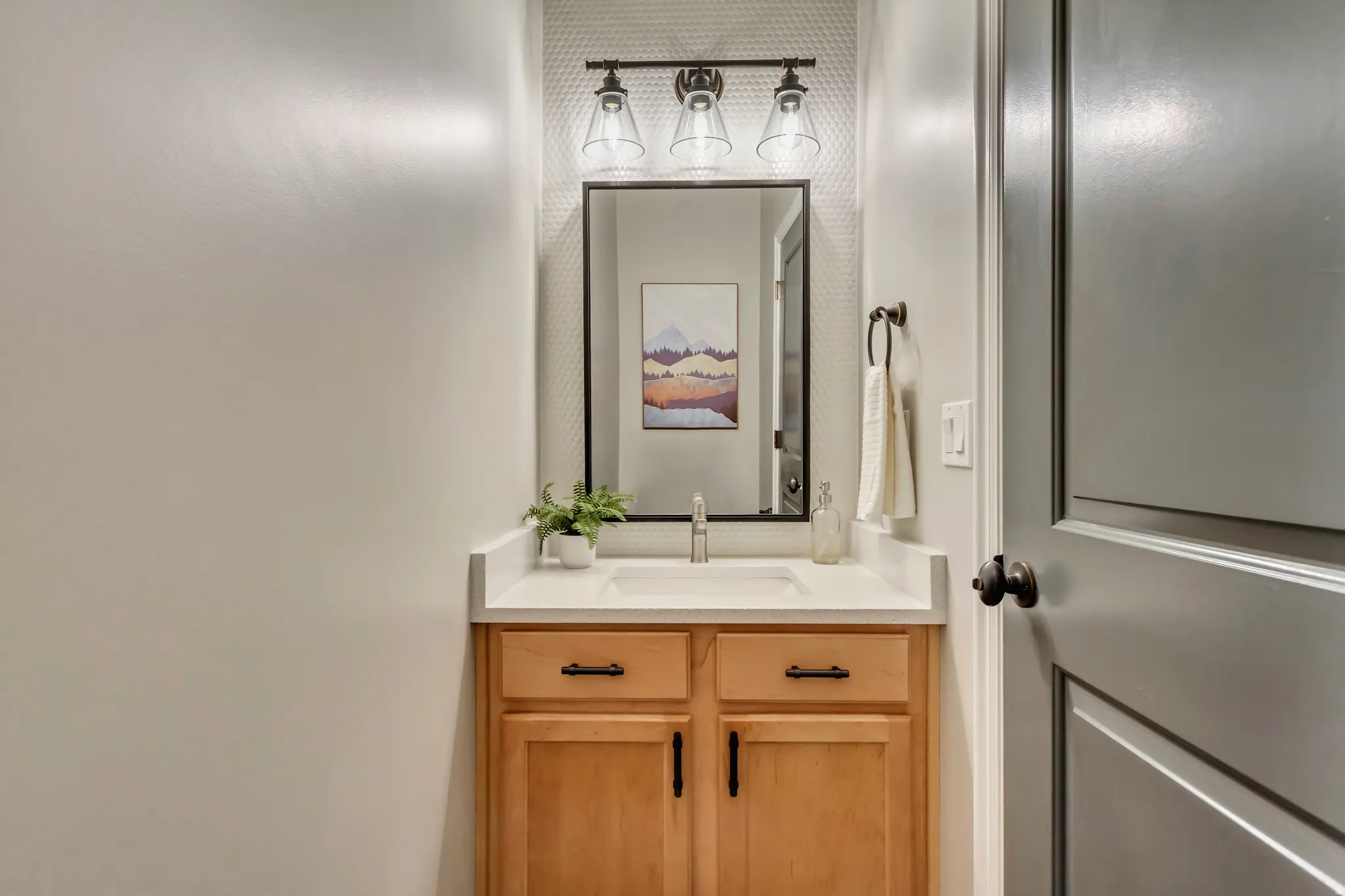 Half Bathroom vanity featuring a light wood-finish cabinet with black hardware, a light-toned countertop, and an undermount sink