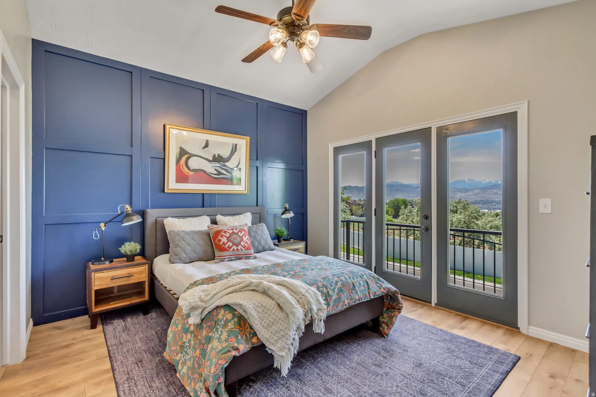 Bedroom featuring a vaulted ceiling, accent wall with molding, door with balcony and wood-finish flooring