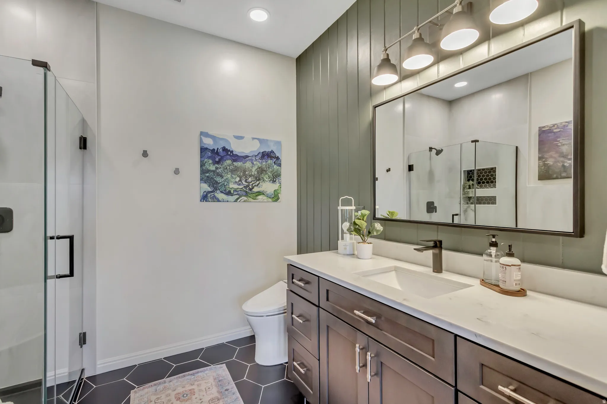 Modern bathroom featuring a glass-enclosed shower with matte black hardware, a dark wood-finish vanity with a quartz countertop, a rectangular undermount sink, shiplap wall feature and a black-framed mirror illuminated by a four-light fixture