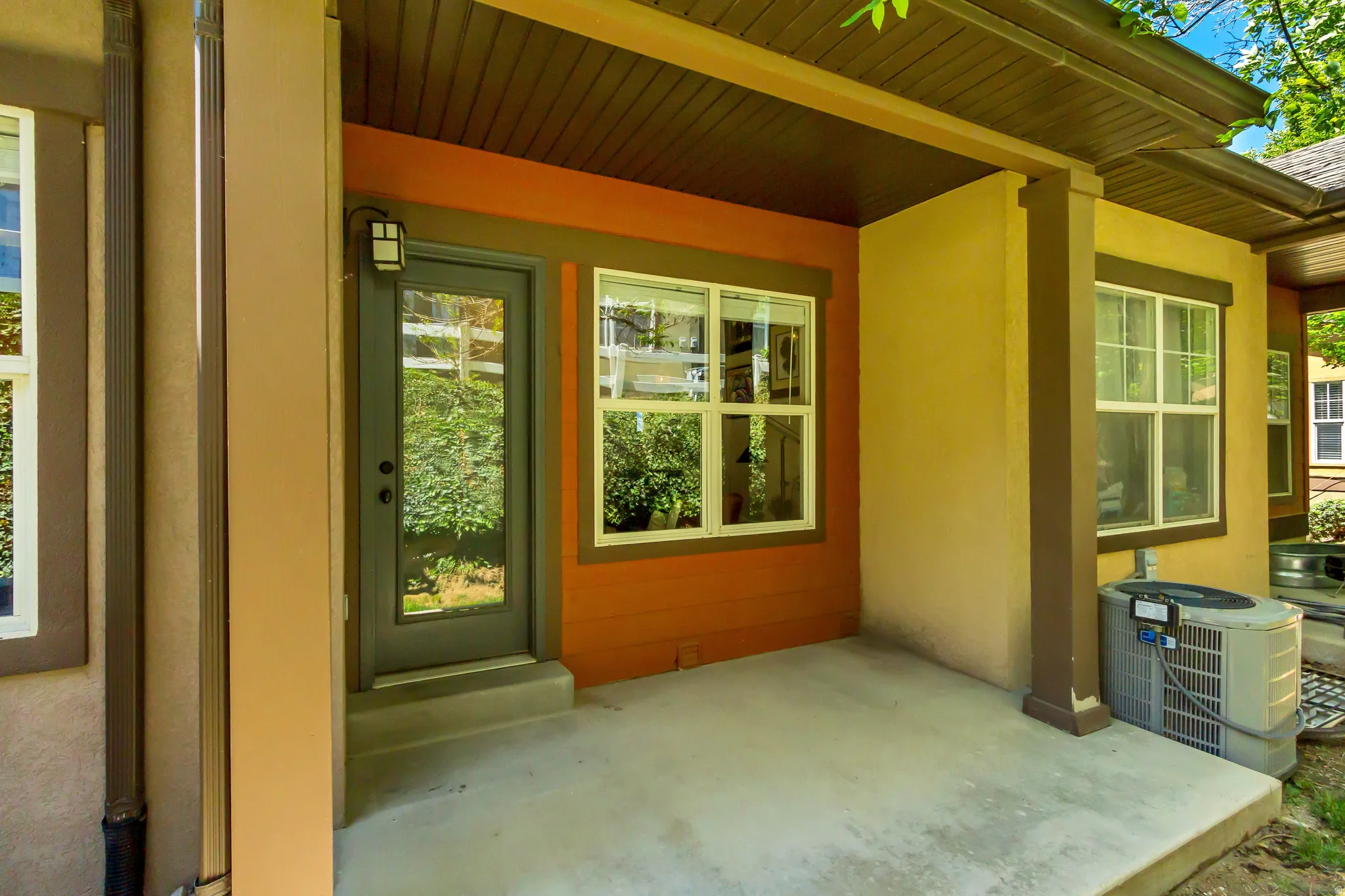 Covered concrete patio with a full-light entry door, exterior wall lantern, and multiple windows