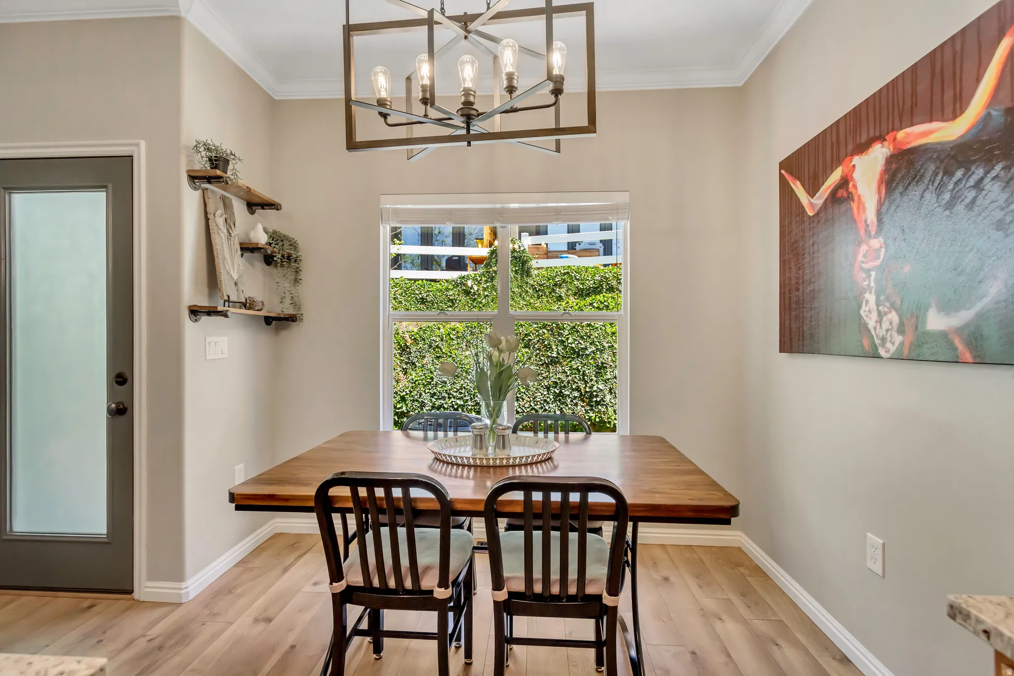 Dining area featuring wood-finish flooring, a contemporary chandelier, a window with exterior foliage, crown molding, and built-in wall shelving