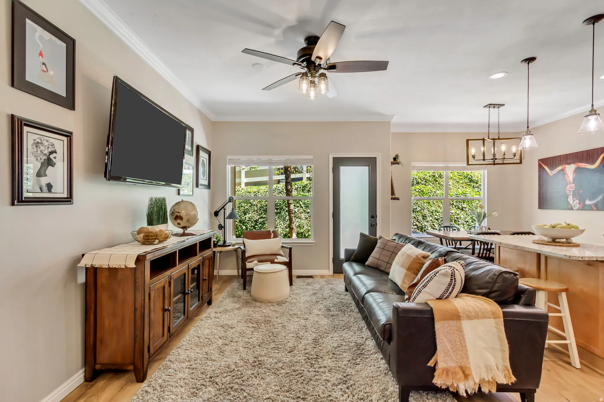Open-concept living area featuring wood-finish flooring, light neutral wall tones, crown molding, and a ceiling fan