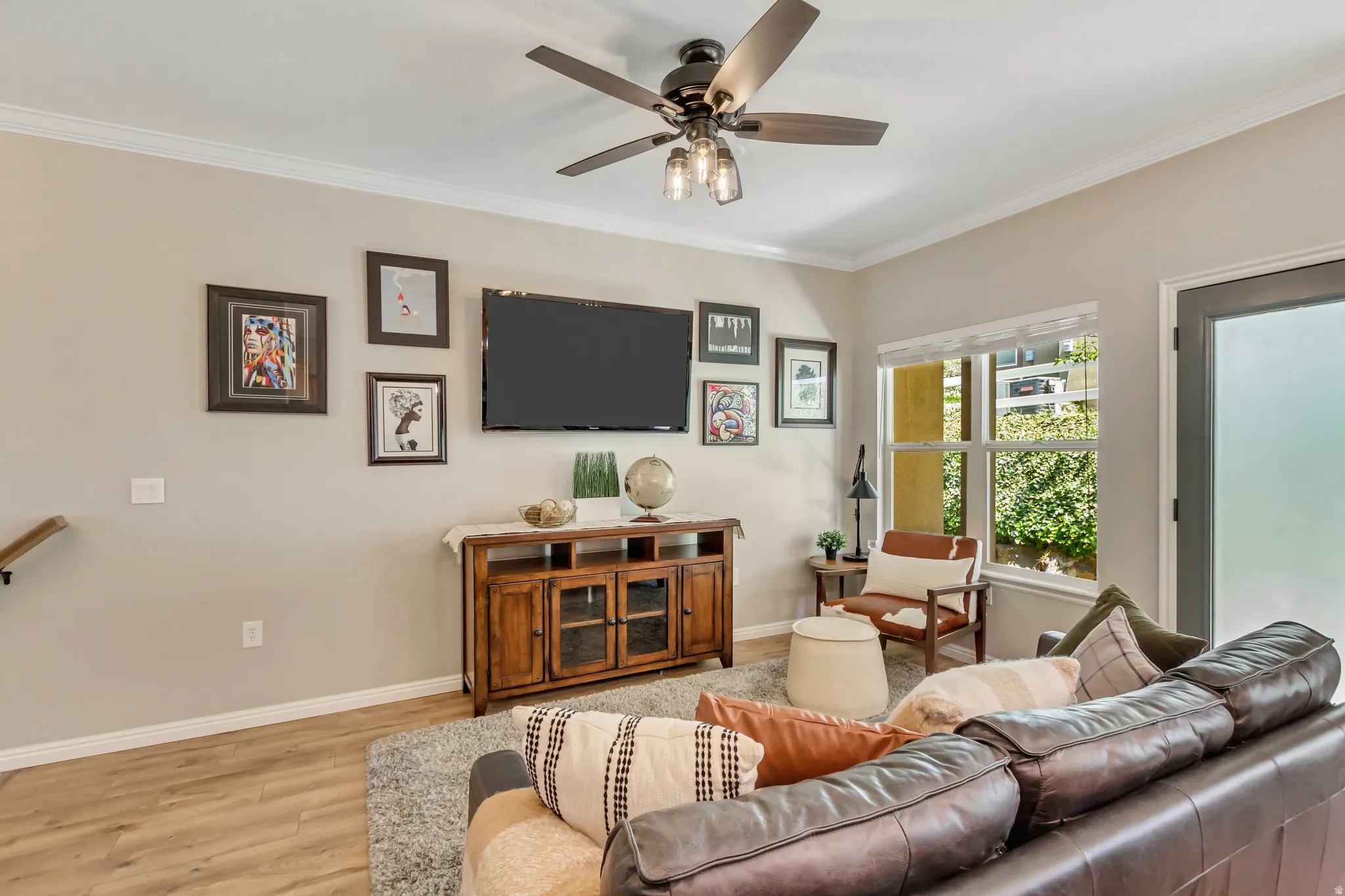 Spacious living area featuring wood-finish flooring, a contemporary ceiling fan, and crown molding