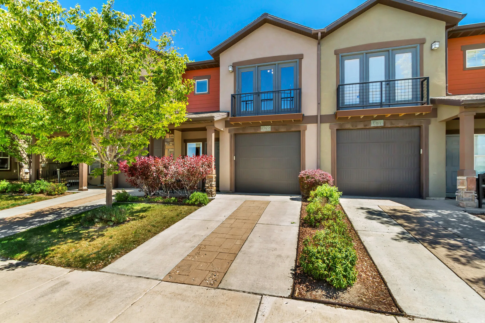 Contemporary townhome exterior featuring a stucco facade, integrated garage, and a second-story balcony with metal railing