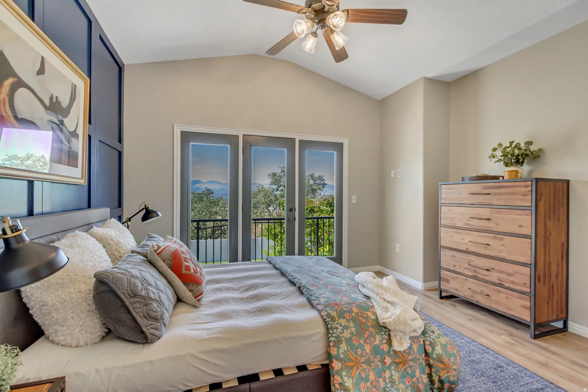 Bedroom with vaulted ceiling, French doors opening to a balcony, wood-finish flooring, door to balcony and a ceiling fan with integrated lighting