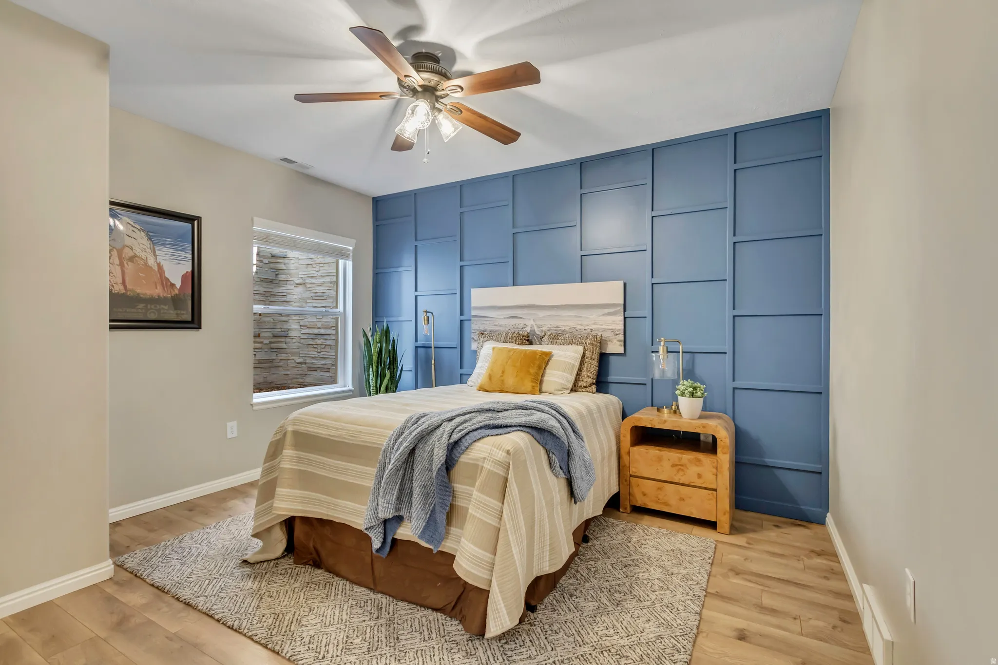 Second primary suite featuring a blue accent wall with geometric paneling, wood-finish flooring, and a ceiling fan with wooden blades
