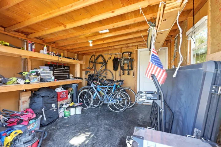 Utility shed featuring wood paneling, exposed wood ceiling beams, built-in shelving, a window, and a white door